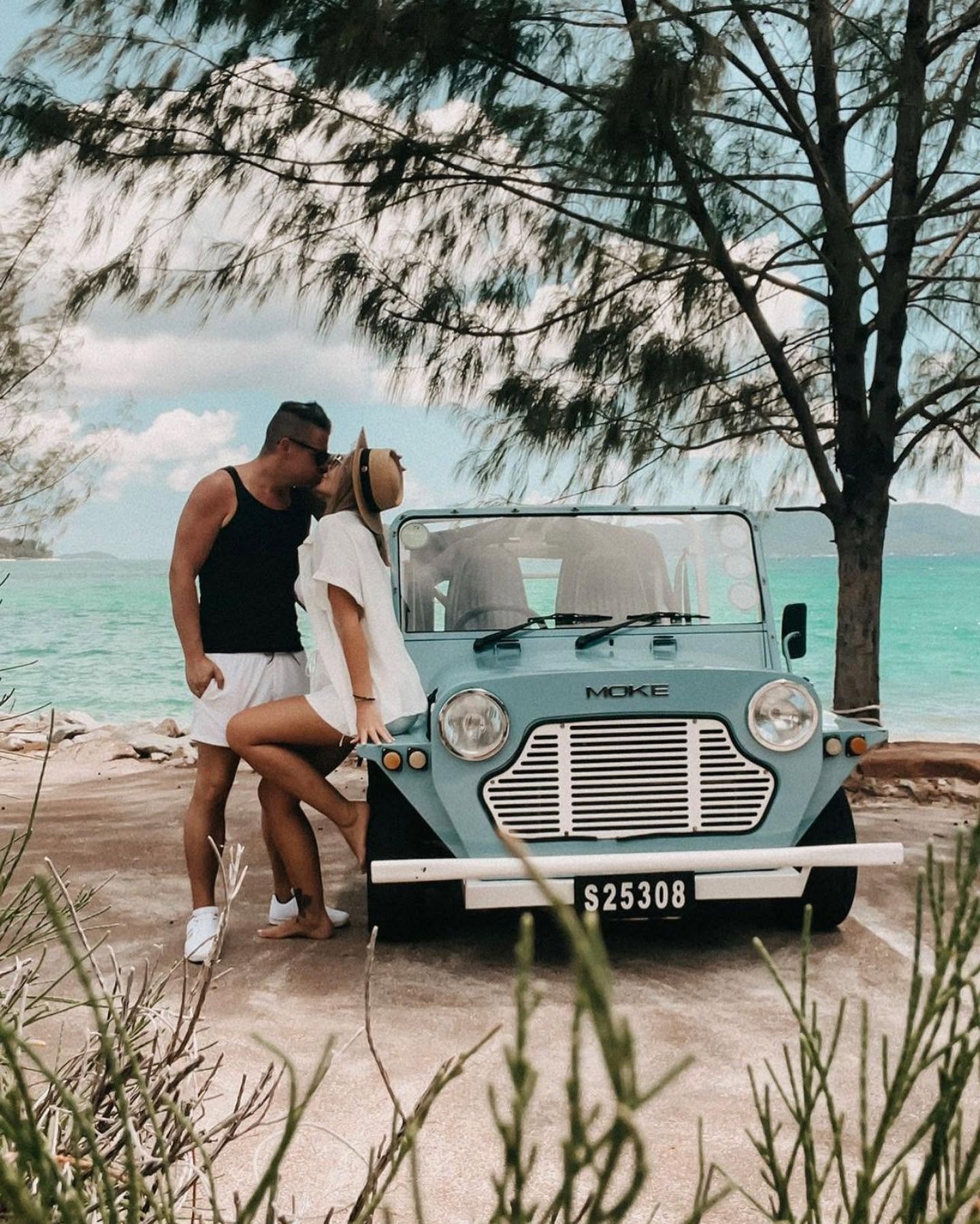 En lyseblå Mini Moke holder på en betonrampe ved kanten af en turkis bugt
