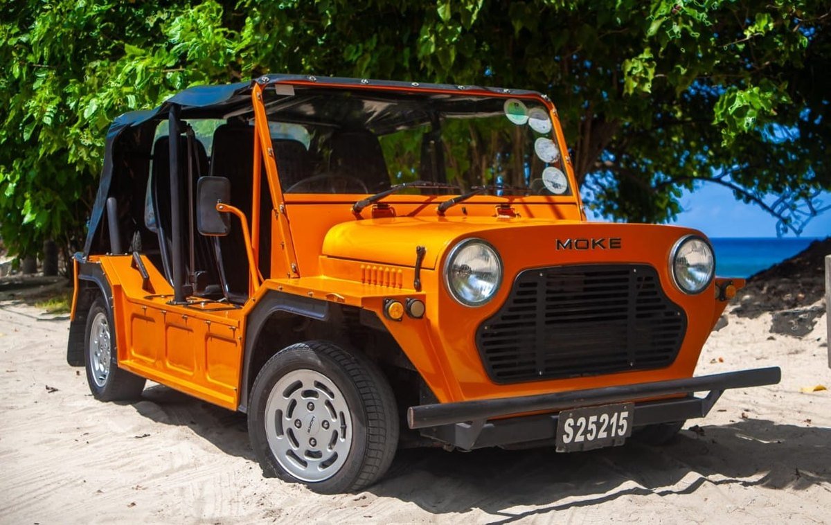 En orange Mini Moke i sandet under takamakatræer