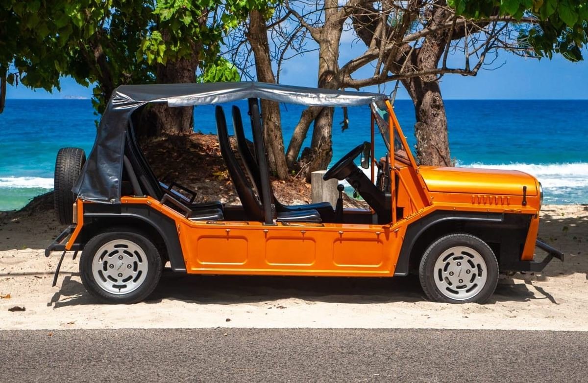 Den orange Mini Moke set fra siden med kalechetaget oppe ved stranden