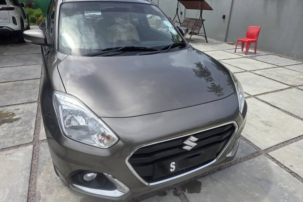 En bronzefarvet Suzuki Dzire set forfra på en indkørsel