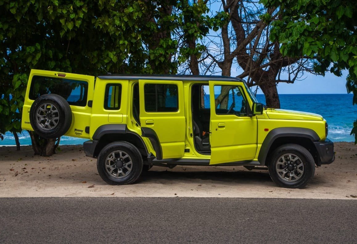Den gule Suzuki Jimny set fra siden med en bagdør åben ved stranden