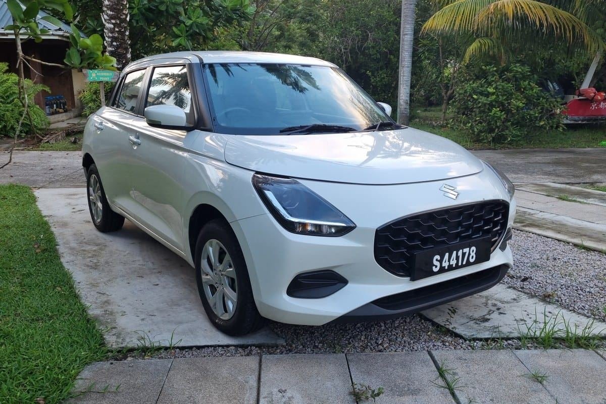 Suzuki Swift parkeret under palmer, set skråt forfra