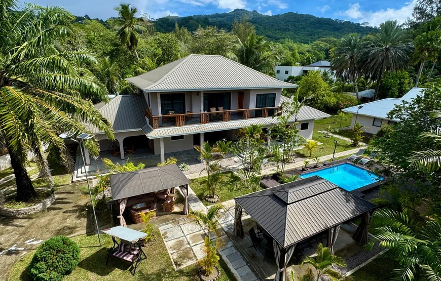 Alibel Beach Villa set fra luften: hovedhuset i to etager, flere mindre huse omkring en pool, palmer hele vejen rundt og en grøn bjergside bagved