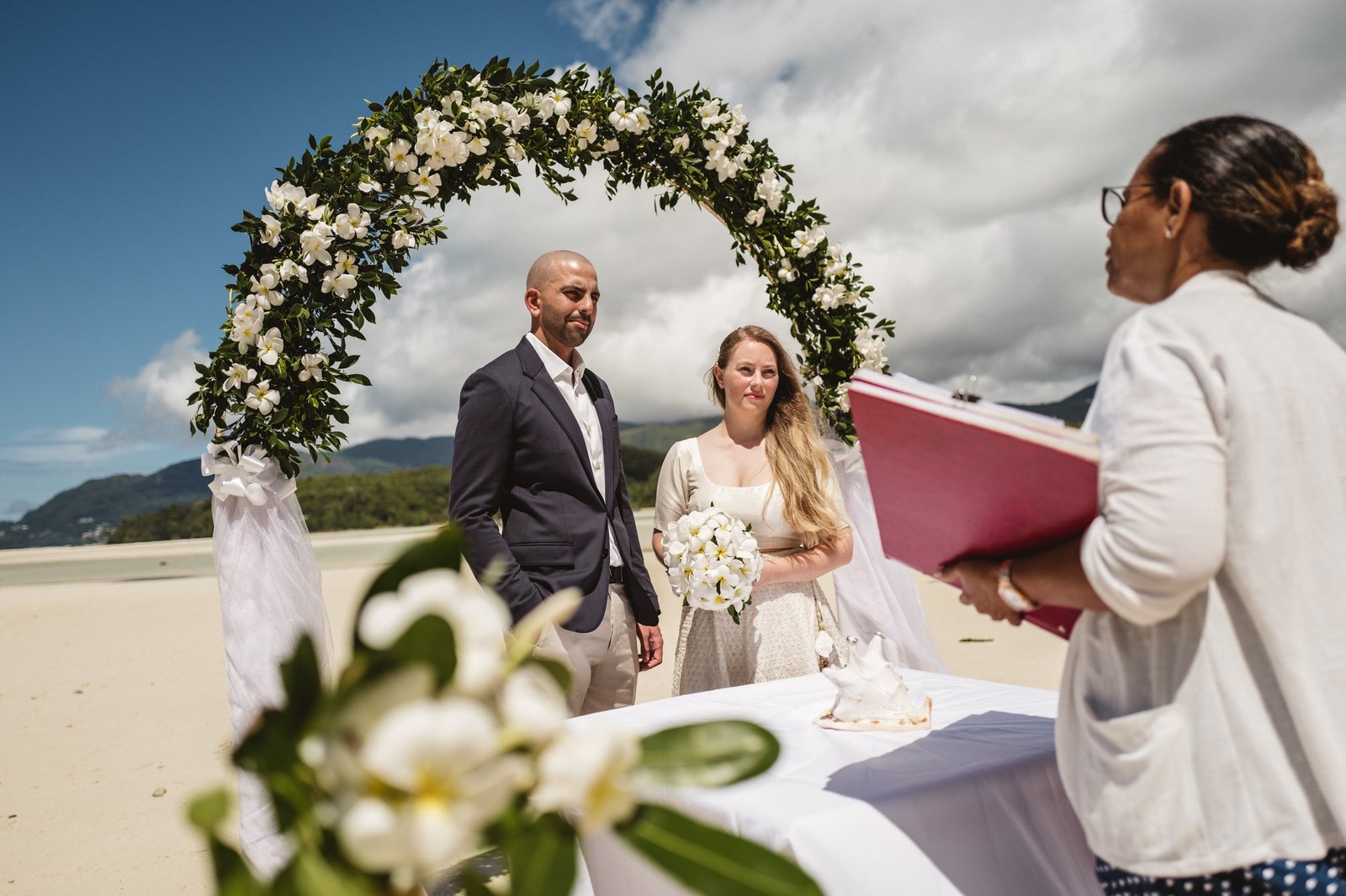 Vielsesforretteren under en blomsterbue på stranden
